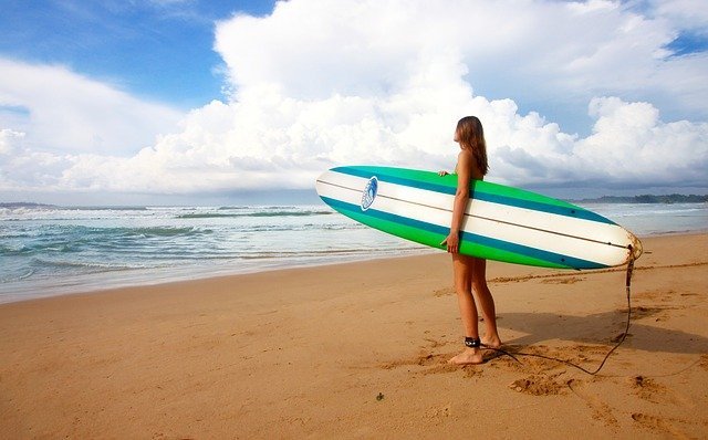 Mujer sosteniendo una tabla de surf y mirando hacia la playa